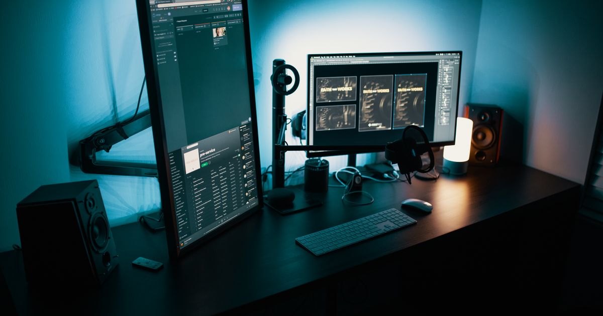 A dark desk with two monitors glowing in blue light